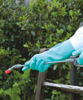Person wearing Heavy Duty Chemical Resistant Nitrile Gloves With Cotton Flock Liner, 15 Mil Thick, using spray bottle outdoors