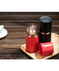Portable Manual Coffee Grinder And Brewer With Built In Bean Storage All In One Travel Coffee Cup, red and black, on wooden tray.