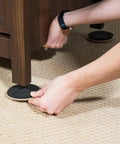 Person placing Heavy Duty Furniture Sliders 8 Pack Moving Pads under a wooden furniture leg on carpet for easy gliding.