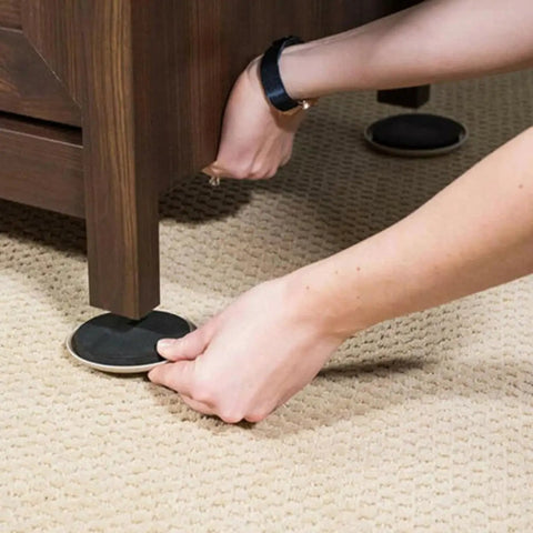 Person placing Heavy Duty Furniture Sliders 8 Pack Moving Pads under a wooden furniture leg on carpet for easy gliding.