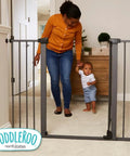 Parent and child near extra tall and wide pressure mounted baby gate for doorways, graphite finish, hallway setting.