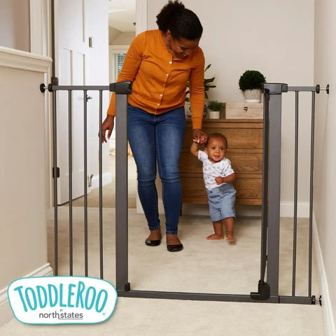 Parent and child near extra tall and wide pressure mounted baby gate for doorways, graphite finish, hallway setting.
