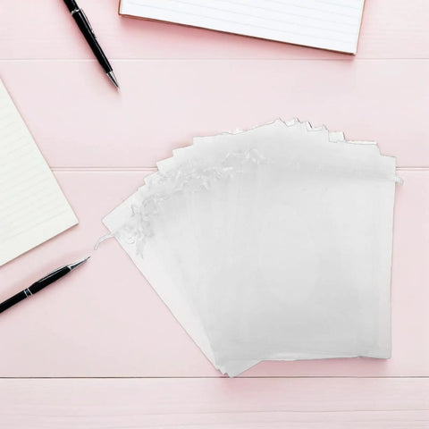 White Organza Drawstring Favor Bags Pack Of 100 Reusable Mesh Pouches for gifts on a pink desk background