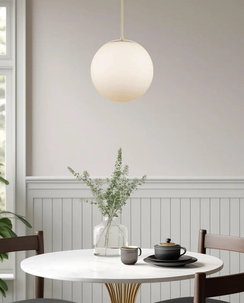 Ceres 14-Inch Mid Century Modern Globe Pendant Light With Frosted Glass Orb Warm Brass Finish above dining table
