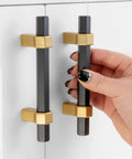 Hand holding Ten Pack 3 Inch Hole Center Black And Gold Cabinet Pulls Matte Black Hexagon Bar With Brushed Gold Bases on white cabinet