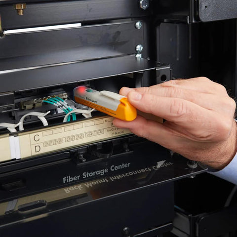Close-up of FiberLert-125 fiber optic tester/detector (orange/gray) held near fiber cables