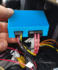Front view of blue rectangular optic fiber decoder module with plugged-in wiring harnesses in a car dashboard
