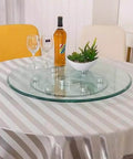 Clear Tempered Glass Lazy Susan Turntable With Silent Bearings And Six Smooth Rolling Wheels For Effortless 360 Spin On Your Kitchen Or Dining Table Making Serve Up Meals A Total Breeze At Home on a table with wine and decorations.