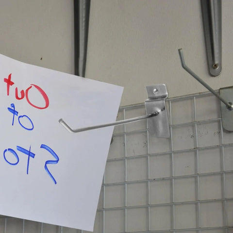 Heavy Duty Slatwall Hooks for Retail Displays holding paper on a grid wall in a store setup