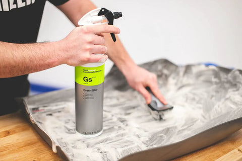 Person cleaning a rubber mat with a spray bottle and brush using All In One Car And Workshop Universal Cleaner Highly Concentrated And Dilutable.