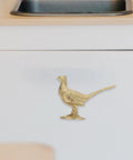Top Shelf Brass Pheasant Drawer Knob With Rich Golden Finish, decorative bird hardware on white cabinet.