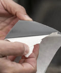 Hands holding Heavy Duty Waterproof Repair Tape, peeling backing, showing adhesive side. 2 inch by 5 foot roll in black color.