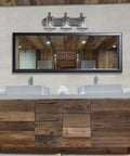 Darby 3-Light Bathroom Vanity Light Fixture In Weathered Iron With Clear Seedy Glass Shades above rustic wood vanity in bathroom.