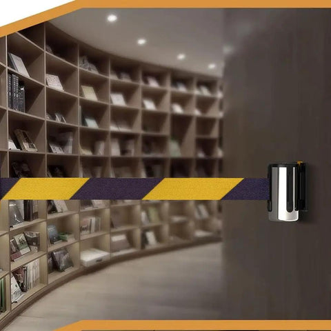 Slick Wall Mounted Retractable Warning Belt With Auto Magnetic Lock, Built Tough Five Meter Yellow And Black Barrier mounted in a library.