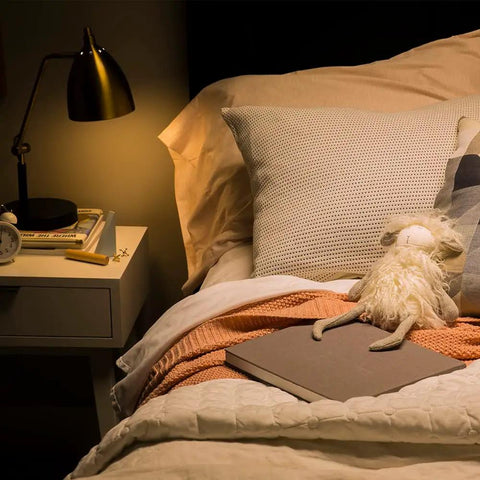 Cozy bedroom with lamp illuminating pillows and toys, featuring Relax LED A19 Soft White Light Bulbs 40W Equivalent for warm glow.