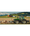 Green tractor in a rural farm setting with cows and mountains in the background.
