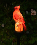 Red Bird Solar Light Garden Stake Figurine in garden glowing at night, weather-resistant for outdoor yard decor and memorial gift.