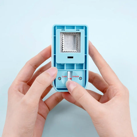 Hands holding a blue Rectangular Postage Stamp Punch 1x0.8 Inch With Scalloped Edge, showing lock and unlock buttons, ideal for crafting.