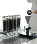 Single Dose Coffee Bean Storage Tubes, Glass And Aluminum Vials, Fourteen Piece Set With Acrylic Board in use, showcasing coffee bean dispensing.