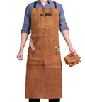 Person wearing Rugged Heat Resistant Welding Apron With Six Tool Pockets, Heavy Duty Leather Forge Apron For Metalworking, holding gloves.