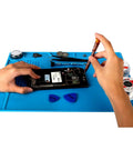 Hands repairing electronics on S-130 Heat Resistant Silicone Soldering Mat For Electronics Repair, blue with tools, 13.8 by 9.8 inch