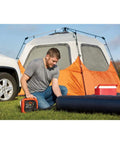 Man using 12V DC Multipurpose Inflator With Digital Gauge, High-Volume For Air Mattresses And Rafts, near camping tent and air mattress.