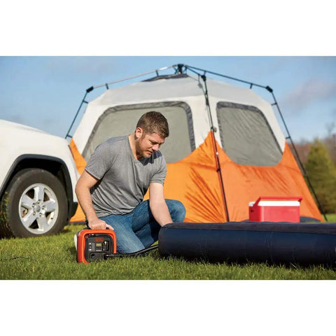 Man using 12V DC Multipurpose Inflator With Digital Gauge, High-Volume For Air Mattresses And Rafts, near camping tent and air mattress.
