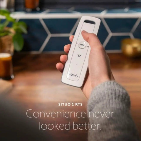 Using the Situo Pure II RTS Single Channel Remote Control For One Motorized Shade Or Gate in hand, rustic kitchen background.