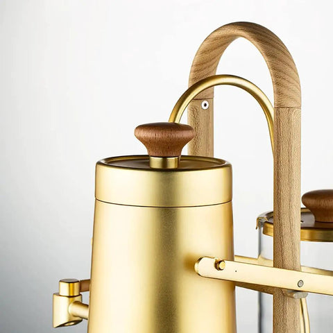 Top Shelf Belgian Siphon Coffee Maker With Stunning Gold Finish Built From Heavy Glass And Steel Frame Relies On Steam Heat And Gravity Action To Pull Silky Smooth Brews Fast Sick Flex For True Coffee Geeks Wanting Elite Taste At Home Or Work, featuring gold body and wood accent.