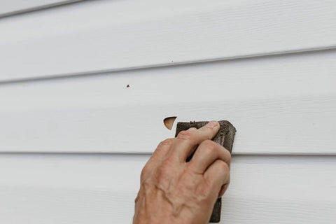 Hand applying Vinyl And Stucco Siding Repair Kit With White Self Adhesive Patches That Cut To Fit Paintable To Match Cover Cracks Holes And Blemishes Weather Resistant Indoor Outdoor Use Includes 2 Patches on siding.