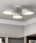 White semi flush mount ceiling light with three metal shades in a modern design, in a room setting.
