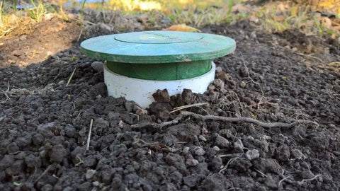 Pop Up Drainage Emitter With Elbow For 4 Inch Drain Pipe in-ground installation with green cap, lawn surface view