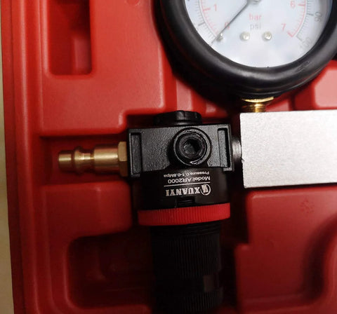 Cylinder leak-down tester for engines; red housing with brass connector and visible pressure gauge (close-up view).