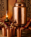 Copper Hammered Water Dispenser Tank with Tap, 6.5 Liter Capacity, Pure Copper Interior, five matching glasses on a table