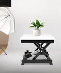 Sturdy Electric Scissor Lift Table With Remote And Manual Control Holds 130 Lbs For Easy Material Handling In Garage And Warehouse Plus Foldable Hydraulic Platform Adjusts Height From 7.17 To 16.14 Inches with white tabletop and plant.