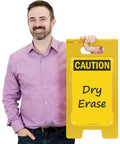 Blank Caution Folding Floor Sign 25 By 12 Inches Double Sided Dry Erase Plastic Sign With Built In Handle Write On Surface Grab And Go Portable Durable Great For Temporary Hazards And Safety Messages. Man holding yellow dry erase caution floor sign with handle