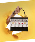 Front view of a small black clutch with white ruffle trim, red decorative rivets, and gold accents; top handle.