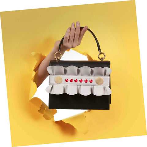 Front view of a small black clutch with white ruffle trim, red decorative rivets, and gold accents; top handle.