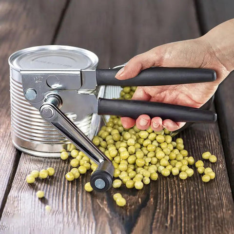 Heavy Duty Manual Can Opener With Rubber Coated Long Handles, Commercial Grade Squeeze And Crank Can Opener For Kitchen, Restaurant, And Outdoor Picnics, Durable Stainless Steel Body, Easy Grip, Long Lasting Performance in use opening a can on wooden table.
