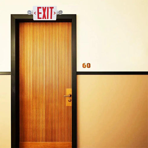 Red LED Exit Sign With Emergency Lights And Battery Backup, Dual Adjustable Head LED Lamps, above a wooden door in hallway.