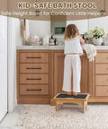 Child using wooden stool at bathroom vanity with storage cabinets underneath