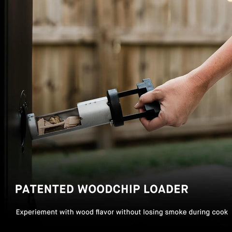 Hand placing wood chips into loader of Digital Electric Vertical BBQ Smoker With Patented Side Wood Chip Loader And Chrome Racks 710 Square Inches