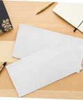 White Pro-Grade Self-Sealing Security Mailing Envelopes 115mm X 225mm on a wooden desk with pens and notebooks.