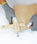 BESTNULE leather cutter with wooden handle and metal clamp cutting beige leather, close-up view