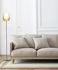 Living room with beige sofa and floor lamp near white paneled walls, showcasing clean and elegant decor.