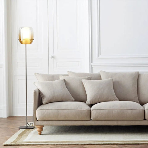 Living room with beige sofa and floor lamp near white paneled walls, showcasing clean and elegant decor.