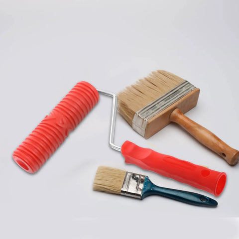 Red Grain Pattern Paint Roller For Wall Texturing With Ergonomic Plastic Handle alongside two paint brushes on a white surface.
