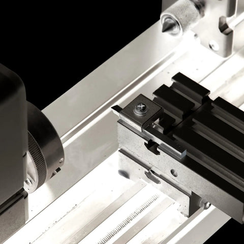 Front view of a miniature metal lathe; cross-slide carriage with T-slots on a silver bed.