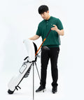 Man holding Golf Swing Trainer Pro Indoor Practice Aid with MAX SPEED Stick next to golf bag in studio setting.