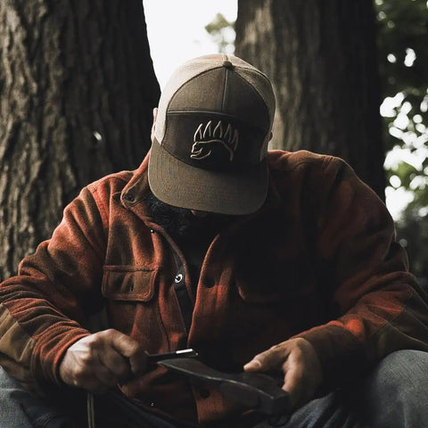 Man using Prepper-Ready Large 6 Inch Ferro Rod With Tungsten Carbide Striker And Sharpener outdoors, wearing flannel and cap